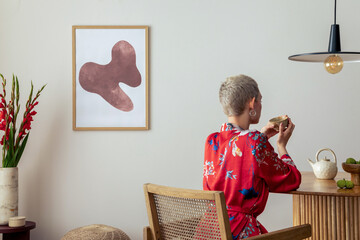 Sunny and bright space of living room with mock up poster frame, woman in red kimono, bouquet...