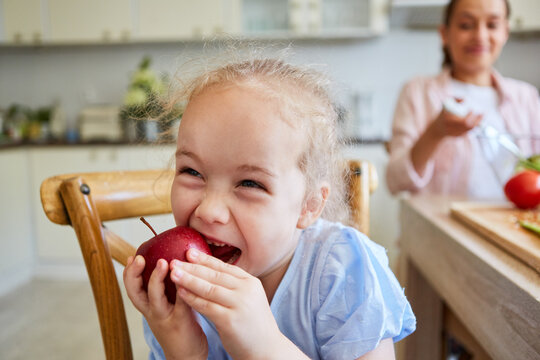 Girl biting apple sitting in kitchen at home