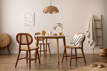 The stylish dining room with round table, rattan chair, wooden commode, poster and kitchen accessories. Beige wall with mock up poster. Home decor. Template.