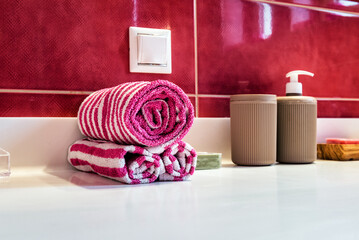 Bathroom detail featuring neatly rolled towels in pink and white stripes. The blurred background showcases vibrant red tiles. Ideal for home decor, interior design inspiration, and lifestyle concepts