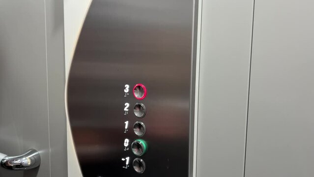 Male hand pressing button in a modern elevator, going up to third level. Interior of silver lift in modern apartment.