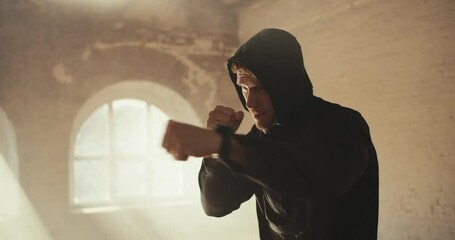 A man with curly hair in a black sports uniform from practicing air strikes in a sunny gym. boxing training