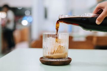 Selective focus shot of pouring out a bottle of beer to a glass with blurry foreground and...