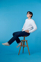 man sitting on a chair look side on blue background
