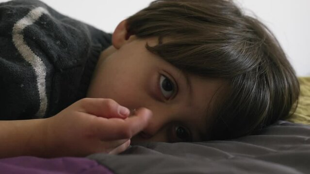 Child picking nose while laid on bed. Kid nose-picking
