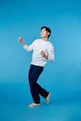 young asian man dancing isolated on blue background