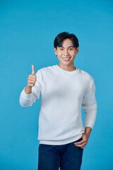 Smiling young asian man wearing white jumper and jeans on blue background giving thumbs up