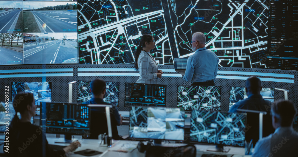 Poster Two Multiethnic Software Engineers Talking Next to a Big Screen in a Modern Monitoring Office with Live CCTV Footage with Traffic Situation. Monitoring Room Big Data Engineers Work on Computers