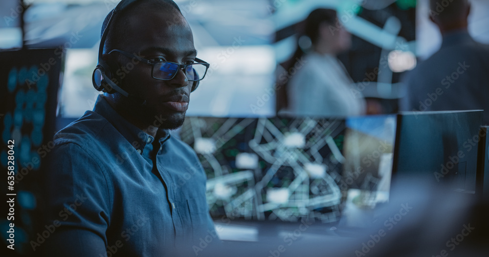 Poster African Specialist in a Dark High-Tech Monitoring Room, Concentrated on a Call and Computer Work. Black Technical Support Manager Using Headphones with Built-In Mic for Communication with Client