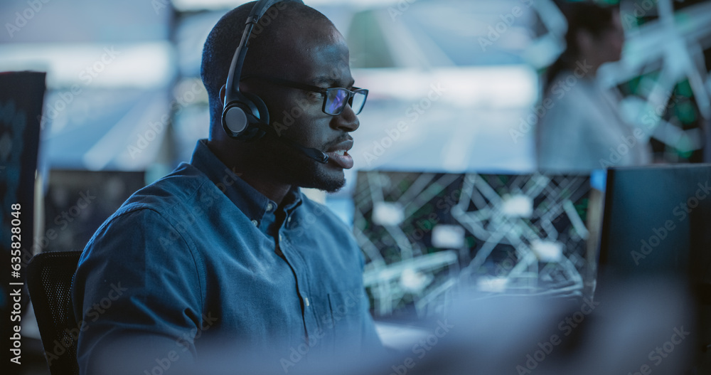 Poster Black Man Effectively Multitasking with Supporting Clients on a Phone Call and Computer Work. Handsome Surveillance Specialist in a Modern Monitoring Room with Displays and Computers