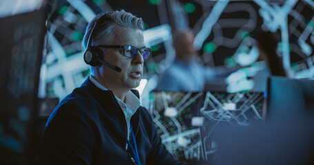 Portrait of a Middle Aged Logistics Officer Wearing a Headset, Working in a Central Office Hub for Delivery Operations, Control and Monitoring for Managing International Fleet of Drivers