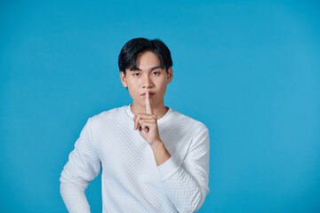 Portrait of serious young Asian man showing a sign of silence gesture putting fingers in mouth