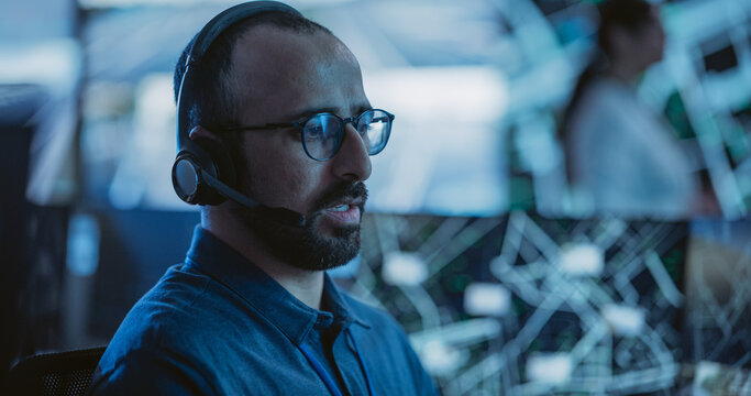 Portrait of a Surveillance Officer Wearing a Headset, Working in a Central Office Hub for Cybersecurity Operations, Control and Monitoring for Managing National Security and Technology