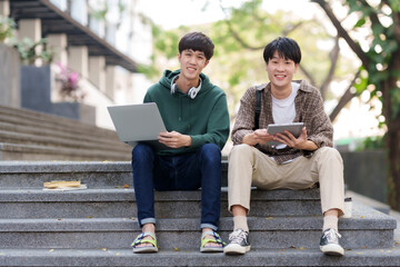 Portrait of two asian man students using tablet and laptop sitting in a university.