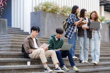 Fototapeta premium Group Of Young Asian Students Collaborating Outdoors at University. Teamwork and Knowledge Sharing. Asian Students Engaged in Collaborative Learning Outdoors.