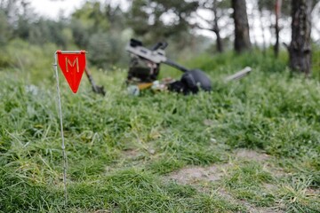 Explosive devices and a metal detector lie on the background of a forest massif. Equipment for demining the territory