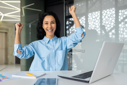 Portrait Of Sleepy Mature Adult Business Woman, Latin American Joyful Winner Looking At Camera Holding Hands Up Gesture Of Triumph And Success, Boss Working Inside Office With Laptop.