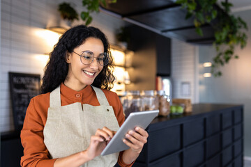 Female barista waitress inside cafe using tablet, latin american restaurant owner smiling using...
