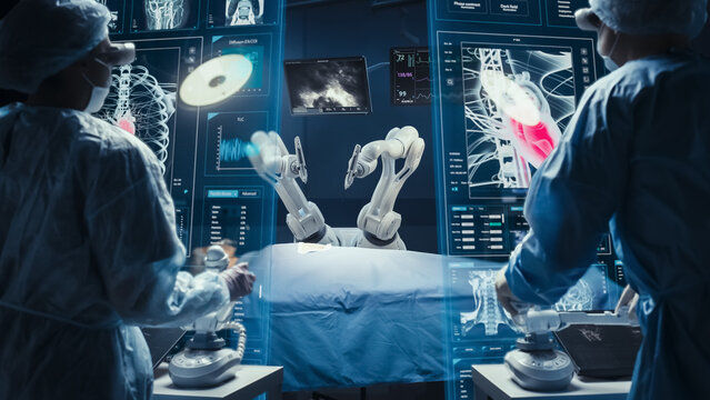 Surgeons Wearing AR Headsets And Using High-Precision Remote Controlled Robot Arms To Operate On Patient In Hospital. Doctors Working With Robotic Limbs, Observing Vitals On Holographic VFX Displays.