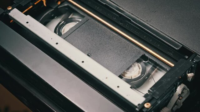 VHS video cassette put inside VCR recorder and playing. Vintage VHS mechanism of videotape insert tape to video head. Old video recorder inside close-up. Concept of playing old video file or movie.