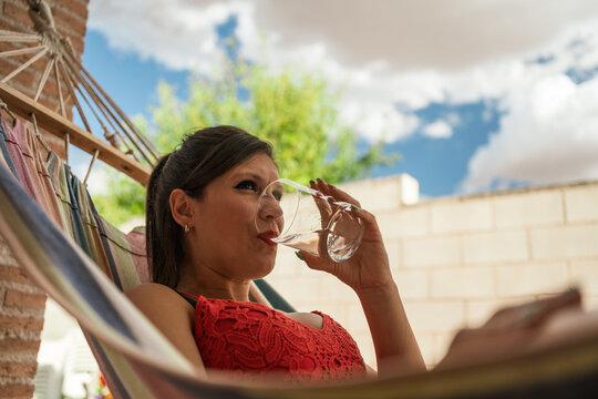 Young girl in a hammock with a glass of water. Frontal image of a brunette woman lying in the backyard hammock teleworking or manipulating the computer on her legs.