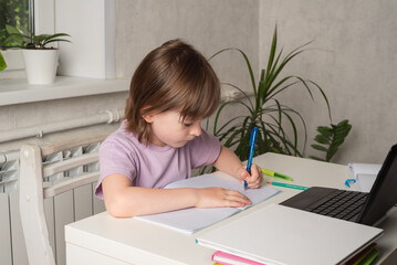 Happy girl sits at a table and works on a laptop and writes with her left hand. Left handed child. International Left Handers Awareness Day