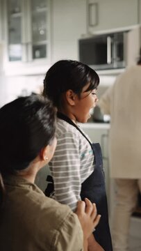 Multi Ethnic Asian Mother Tying Her Daughter's Apron in the Kitchen