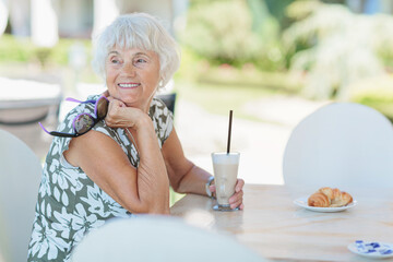 Beautiful senior woman with a cup of coffee with milk resting in nature at the resort in the morning. Vacation, holiday, and travel concept.