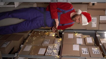 Warehouse worker in santa hat working in storehouse doing inventory using digital tablet - Powered by Adobe