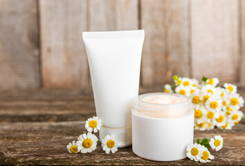 Obraz na płótnie Canvas Open jar of cream for face, body and hands with chamomile flower on a wooden background. Herbal dermatological cosmetic hygiene cream. Natural cosmetic product. Beauty concept. Cosmetic tube.MOCKUP.