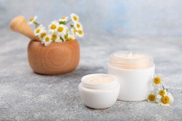 Open jar of cream for face, body and hands with chamomile flower on a blue background. Herbal dermatological cosmetic hygiene cream. Natural cosmetic product. Beauty concept. Cosmetic tube.MOCKUP