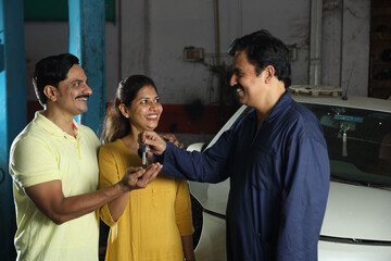 Indian car mechanic delivering the car keys to the happy customers. Portraying customer satisfaction to the whole scene the cheerful car specialist