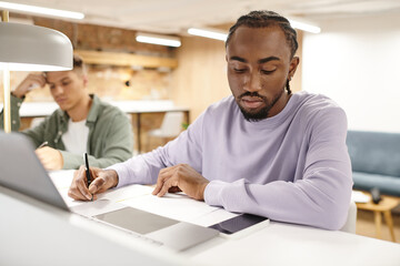 Fototapeta premium coworking, african american man taking notes, writing down ideas near gadgets, startup planning
