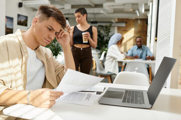 focused man working in office, laptop and documents, paperwork, graphs, coworking, gen z colleagues