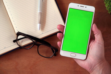 A woman's hand holds a white smartphone with a green screen, shopping, business, work, study