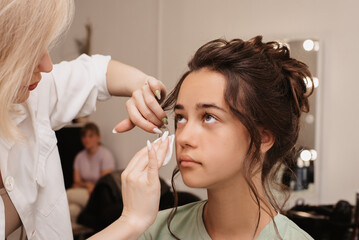 Shooting in a beauty salon. A master makeup artist cleanses the model's skin before applying makeup.