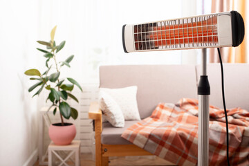 Electric infrared heater warming up living room with sofa and potted plant at background