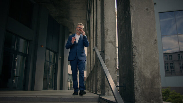 Caucasian mature old man businessman senior business employer walking outdoors on stairs near office building talking phone check time looking at wrist watch late rush hurry worried running lateness