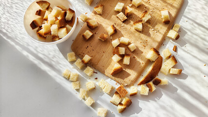 Homemade slices of diced dry white rye bread on cutting board and white plate. Crackers for food, healthy eating on table in sunny day, top view
