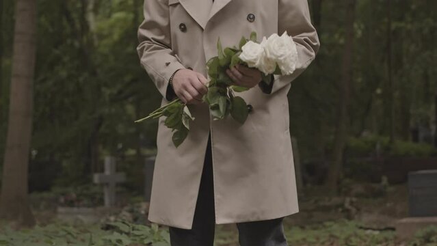 Unrecognizable widower bringing bouquet of white roses to grave of his beloved wife