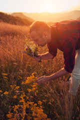 Man picking and holding field flowers in nature.