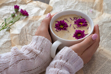 Fototapeta na wymiar Female hands holding a cup of cappuccino with flowers on a book background