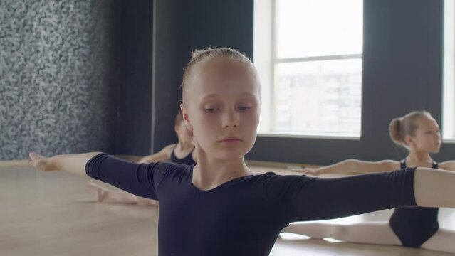 Tilt down shot of girls doing exercises with their arms while sitting in splits during gymnastics classTilt down shot of girls doing exercises with their arms while sitting in splits during gymnastics