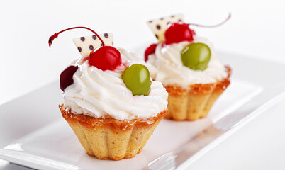 Beautiful cream cakes with cherries and grapes on a plate on a white background