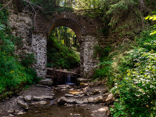 Picturesque ruins of the narrow-gauge viaduct carriage bridge in the village of Vorokhta, Carpathian Mountains, Ukraine. Old stone arched destroyed bridge over small river in a mountain forest.