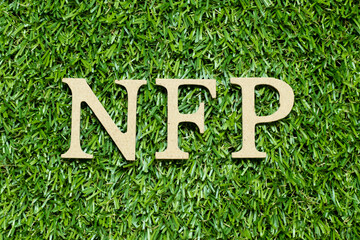 Wood alphabet letter in word NFP (Abbreviation of Nonfarm payrolls) on green grass background