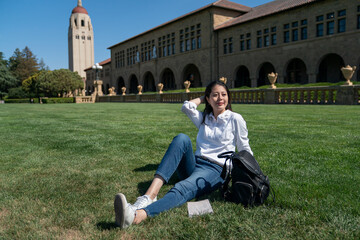 leisure asian korean woman college student pushing hair back and enjoying good weather while relaxing on grass in front of the hoover tower on school campus in California usa