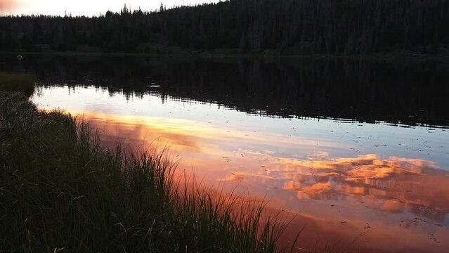 View of the sunset reflecting on the water's surface at the edge of a lake in Utah.