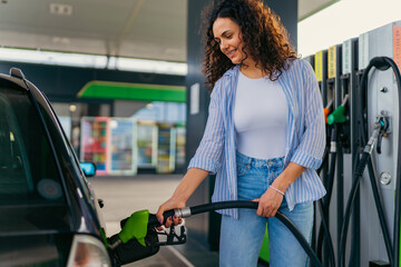 A beautiful woman with curly hair is filling her car tank while taking a break on her road trip