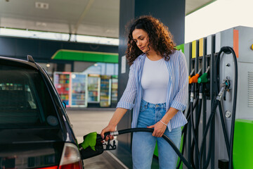 A beautiful woman with curly hair is filling her car tank while taking a break on her road trip
